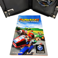 Nintendo GameCube Mario Kart Double Dash instruction booklet in front of an open black GameCube game case, with the game disc visible inside the case on a white background.