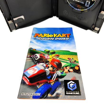 Nintendo GameCube Mario Kart Double Dash instruction booklet in front of an open black GameCube game case, with the game disc visible inside the case on a white background.