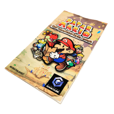 Nintendo GameCube instruction booklet for Paper Mario: The Thousand-Year Door, featuring colorful character artwork of Mario and others on a parchment-style cover, with the GameCube logo at the bottom.