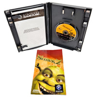 Nintendo GameCube Shrek 2 game case shown open with the game disc inside, alongside the game's instruction booklet featuring Shrek on a warm orange-red background.