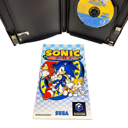 Nintendo GameCube Sonic Mega Collection instruction booklet in front of an open black GCN game case containing the game disc on a white background.