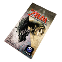 Image of the front of the instruction manual for The Legend of Zelda: Twilight Princess, photographed on a plain white background. The package artwork shows a black wolf on the left and a Link's character portrait on the right, with the title logo in red at the top and a GameCube logo near the bottom.