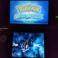 A Nintendo DS console showing the Pokémon Alpha Sapphire game screen, with the game logo on the top display and an underwater scene on the bottom screen.
