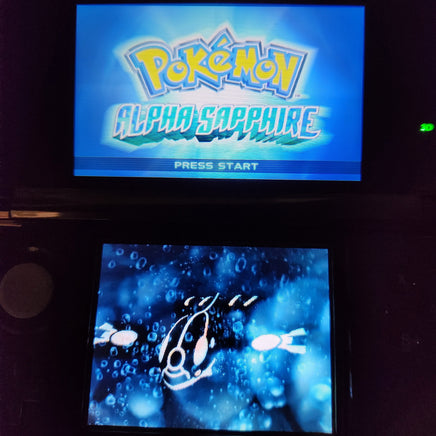 A Nintendo DS console showing the Pokémon Alpha Sapphire game screen, with the game logo on the top display and an underwater scene on the bottom screen.