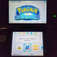 A Nintendo DS handheld console showing the Pokémon Alpha Sapphire game screen on the upper display and the device's interface on the lower screen, photographed against a dark background.
