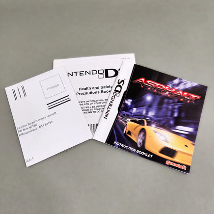Nintendo DS instruction booklet and registration card set for Asphalt Urban GT, featuring a white registration card, a health and safety precautions booklet, and an instruction booklet with a yellow sports car on the cover, displayed on a neutral gray background.