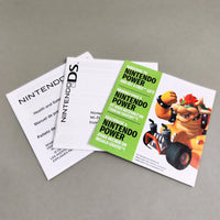 Mario Kart DS for Nintendo DS - Nintendo DS game packaging materials on a neutral gray background, including a white Wi-Fi booklet, a white product card, and a green promotional insert featuring Bowser and the text 'Nintendo Power'.
