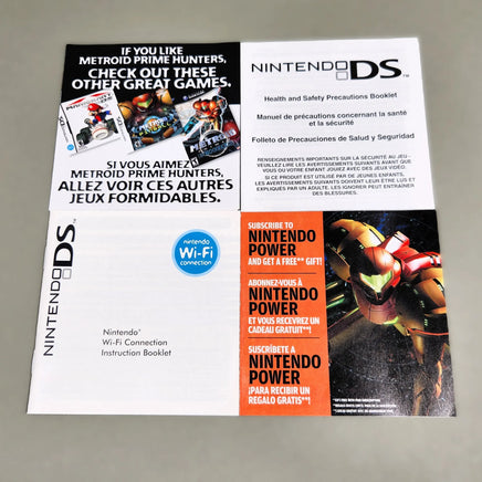 Front view of Nintendo DS printed pamphlets laid flat on a light gray surface: a health and safety booklet, a Wi-Fi connection booklet, and a promotional insert featuring the Nintendo Power logo and a Metroid Prime Samus illustration.