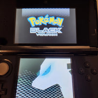 A black Nintendo 3DS handheld game console showing the Pokémon Black Version logo on the top screen and a white Pokémon character on the bottom screen.