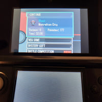A close-up of a Nintendo 3DS handheld game console screen showing the game menu, with a Pokémon badge selection pop-up for Black and Mistralton City visible on the top screen.