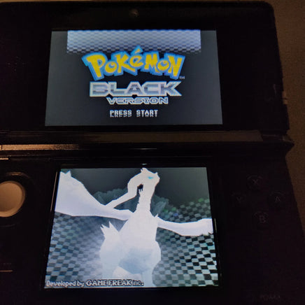 A black Nintendo 3DS handheld game console showing the Pokémon Black Version game menu, with the top screen displaying the Pokémon logo and the bottom screen showing a Pokémon character.