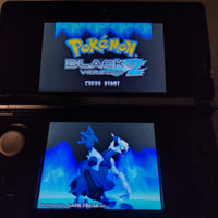 A Nintendo 3DS handheld game console showing the Pokémon Black 2 Version 2 game menu, with the game's icy blue logo on the top screen and a blue-toned character illustration on the bottom screen.