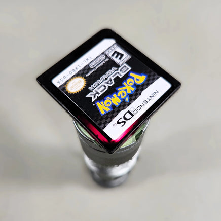 Pokémon Black Version for Nintendo DS - Close-up of Pokémon Nintendo DS cartridge showing reddish-purple translucent shell under light, good condition