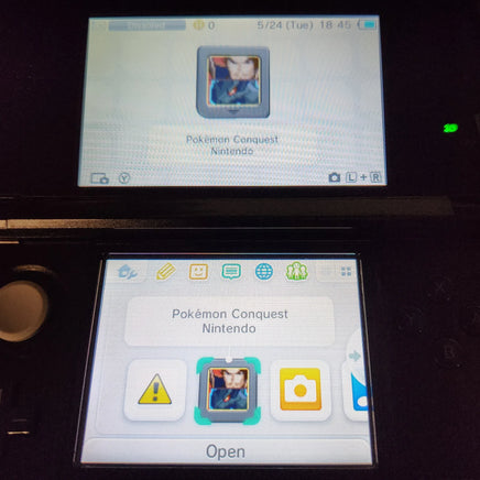 A close-up of a Nintendo 3DS handheld console showing the screen with the Pokémon Conquest Nintendo app open. The top screen displays the app's main interface with a Pokémon portrait, and the bottom screen shows app icons including a warning icon, the portrait, a camera icon, and an 'Open' label.