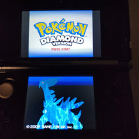 A black Nintendo 3DS handheld console showing the Pokémon Diamond Version game screens, with the Pokémon logo on the top display and a blue dragon-like creature on the bottom screen.