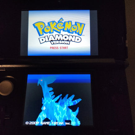 A black Nintendo 3DS handheld console showing the Pokémon Diamond Version game screens, with the Pokémon logo on the top display and a blue dragon-like creature on the bottom screen.