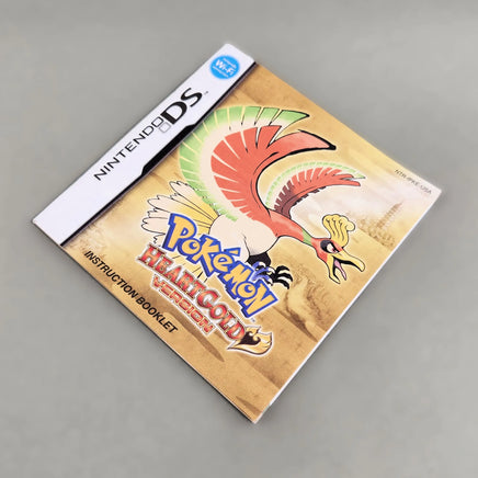 Nintendo DS instruction booklet for Pokémon HeartGold Version, featuring a colorful illustration of Ho-Oh on the cover, photographed on a neutral gray surface.
