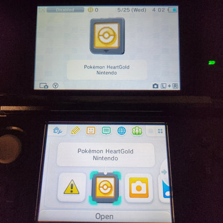A close-up of a Nintendo 3DS handheld console showing the game menu for Pokémon HeartGold on both the upper screen and the lower screen.