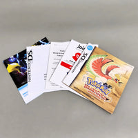 A set of Nintendo DS instruction manuals and booklet covers fanned out on a neutral gray background, including a Pokémon HeartGold Version instruction booklet.