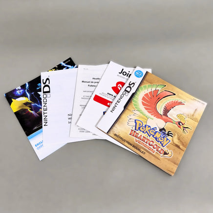 A set of Nintendo DS instruction manuals and booklet covers fanned out on a neutral gray background, including a Pokémon HeartGold Version instruction booklet.