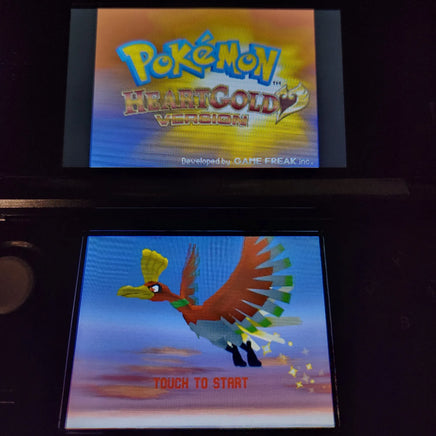 A retro Nintendo DS handheld game console showing the Pokémon HeartGold Version game menu, with the Pokémon logo on the top screen and a flying bird character on the bottom screen with 'TOUCH TO START' text.