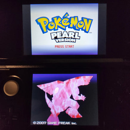 A Nintendo DS handheld game console showing the Pokémon Pearl Version title screen on the top display and a pink creature graphic on the bottom screen, photographed in a dark setting.
