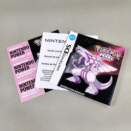 Nintendo DS Pokémon Pearl Version instruction booklet and included papers laid out on a neutral gray surface. The black booklet cover features a large white and purple dragon, with pink and white instruction sheets fanned out behind it.