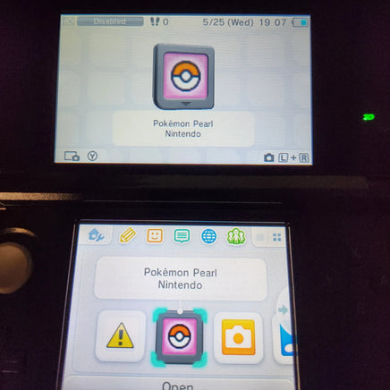 A Nintendo 3DS handheld console showing the Pokémon Pearl Nintendo game icon on its screens, photographed in a dark setting.