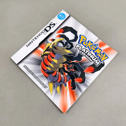 Nintendo DS Pokémon Platinum Version instruction booklet with a character illustration of a metallic scorpion-like Pokémon on the cover, photographed on a plain light gray surface.
