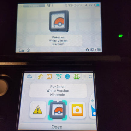 Nintendo DS game screens for Pokémon White Version Nintendo Version, one resting on a dark surface above the other, with their screens turned on displaying the game's interface.