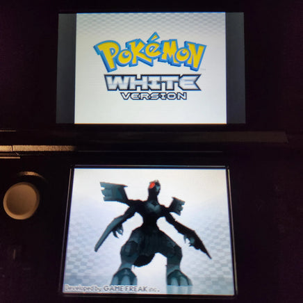 A Nintendo 3DS handheld game console displaying the Pokémon White Version logo on the upper screen and a dark bird-like Pokémon on the lower screen.
