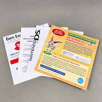 A set of printed Nintendo DS promotional or instruction sheets fanned out on a neutral gray surface. Visible items include a white card reading 'Earn Extra Nintendo Points,' a white card with 'Nintendo DS' branding, and a larger yellow/orange card titled 'Get the Mythical Pokemon Victim!'.
