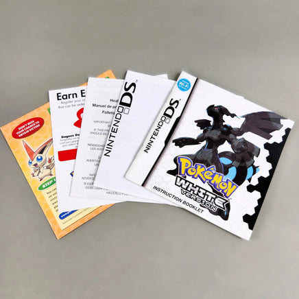 Pokémon White Version 2 instruction booklet and other inserts fanned out on a neutral gray surface, including a white Nintendo DS booklet and a colorful Pokémon booklet.