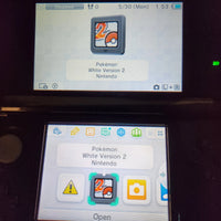 A close-up of a Nintendo 3DS handheld console showing the Pokémon White Version 2 game menu on the screen, with the top and bottom display showing game icons.