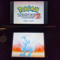 Nintendo DS showing Game Freak game Pokémon White Version 2 menu on its screens, photographed in a dark room.