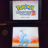 A Nintendo DS handheld game console with the Pokémon White 2 Version 2 game displayed on the screen, showing the game title on the top screen and a blue dragon character on the bottom screen.