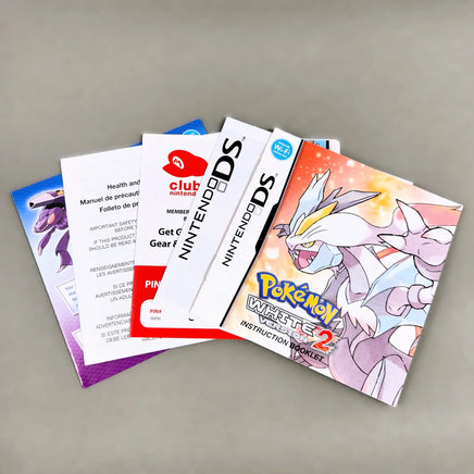 A set of Nintendo DS instruction manuals and pamphlets fanned out on a neutral gray surface. Visible items include a Pokémon White Version 2 instruction booklet, a white Nintendo DS booklet, a Club Nintendo membership card, and other colorful game papers.