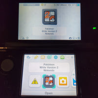 A Nintendo 3DS handheld console showing the Pokémon White Version 2 game interface on both the top screen and the lower screen, photographed in a dark setting.