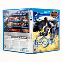 Front and back views of a Nintendo Wii U game case for Bayoneta 2, showing the blue plastic case edges, cover art with a black-winged character, and back panel details on a white background.