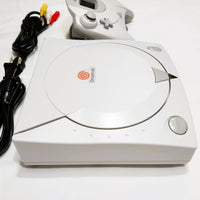 White Dreamcast gaming console with controller and cables on a white background