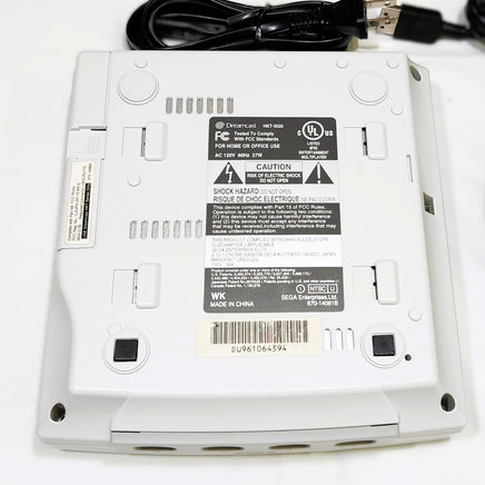 Bottom view of a Sega Dreamcast console with cables on a white background